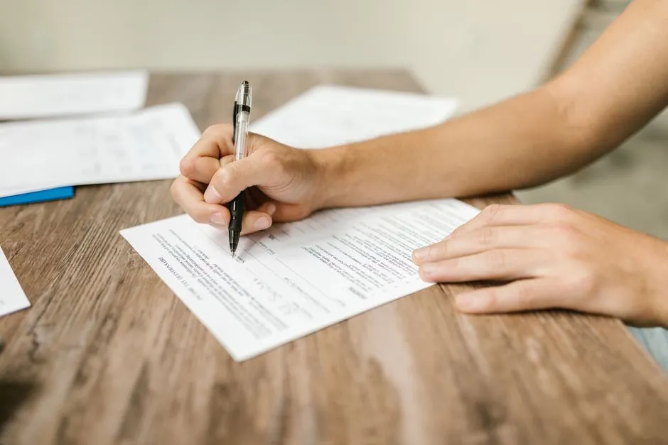 Close-up of a person filling out a paper application form with a pen